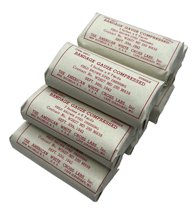  Rolled bandages wrapped in white paper with red printed text reading 'Bandage Gauze Compressed' and 'The American White Cross Labs, Inc.', arranged on a light gray background.