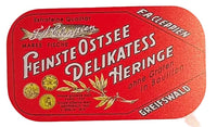 A vintage German fish can label design for 'Feinste Ostsee Delikatess Heringe' by Greifswald, featuring a red rounded rectangle with white lettering and gold fish illustrations on a white background.