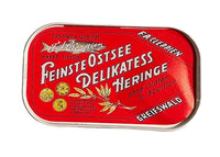 A vintage red metal tin of Fiskeriet Feinste Ostsee Delikatess Heringe, featuring white German text and gold fish illustrations, photographed on a neutral light gray background.