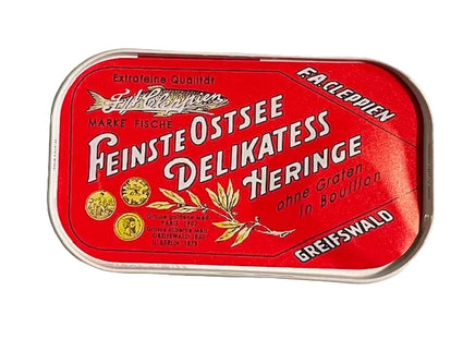A vintage red metal tin of Fiskeriet Feinste Ostsee Delikatess Heringe, featuring white German text and gold fish illustrations, photographed on a neutral light gray background.