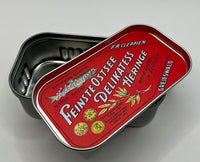 A vintage German fish can, featuring a red lid with white and gold lettering that reads 'Feinste Ostsee Delikates Heringe' and 'F.A.